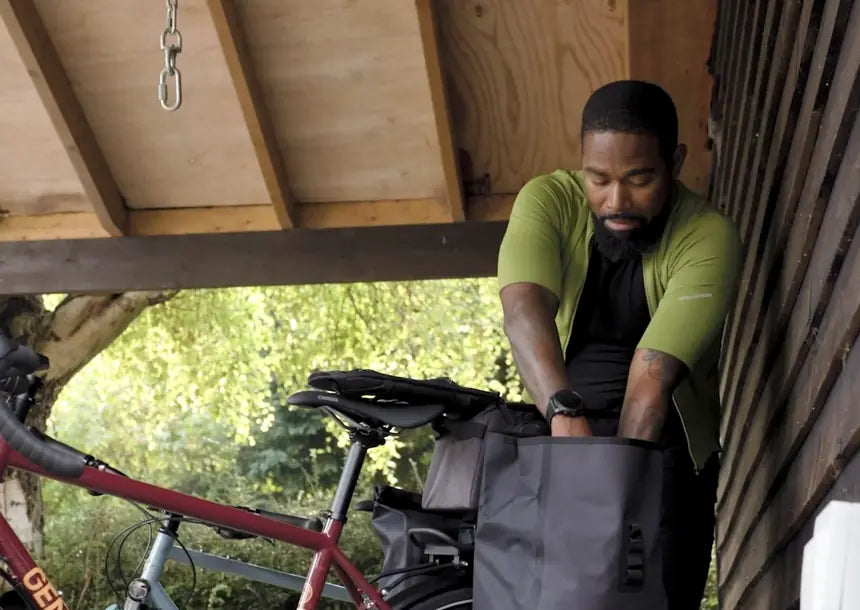 Cyclist loading a waterproof pannier onto a rear rack on a Genesis touring bike, Aztecs Bikes, East London